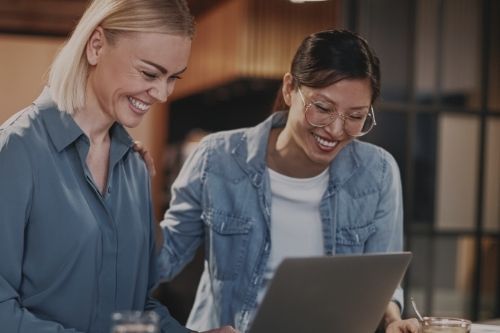 two women smiling in front of laptop