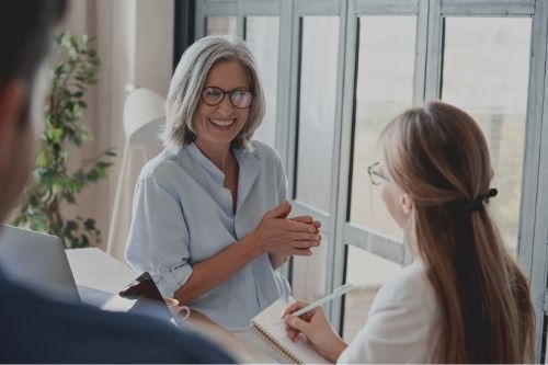 woman with glasses smiling while another woman takes notes